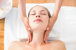 Relaxed woman receiving soothing facial massage while lying on white towel.