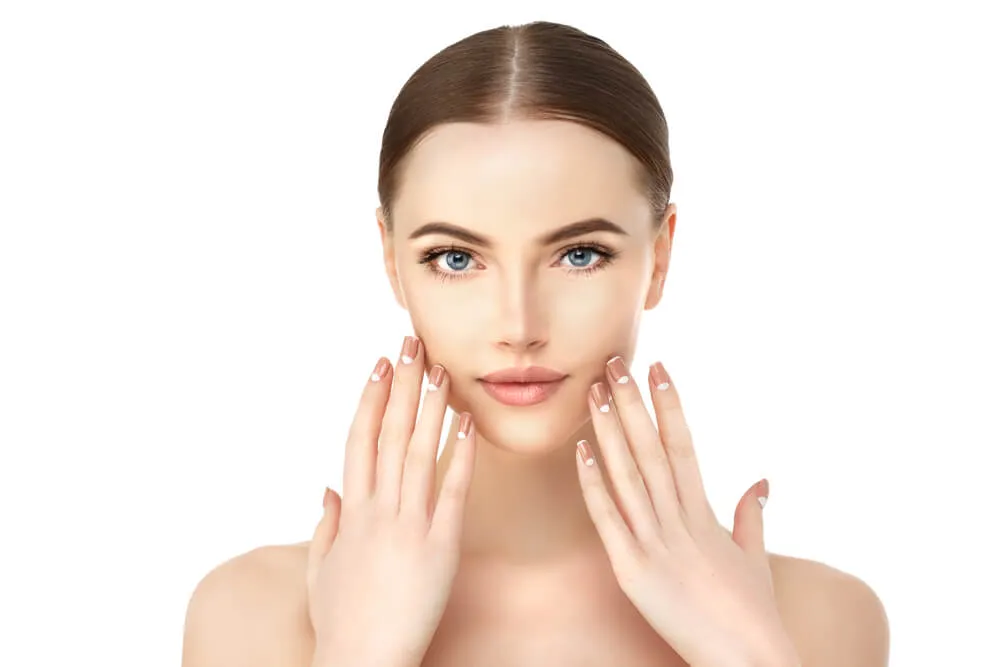 Woman with clear skin touching face gently with both manicured hands.